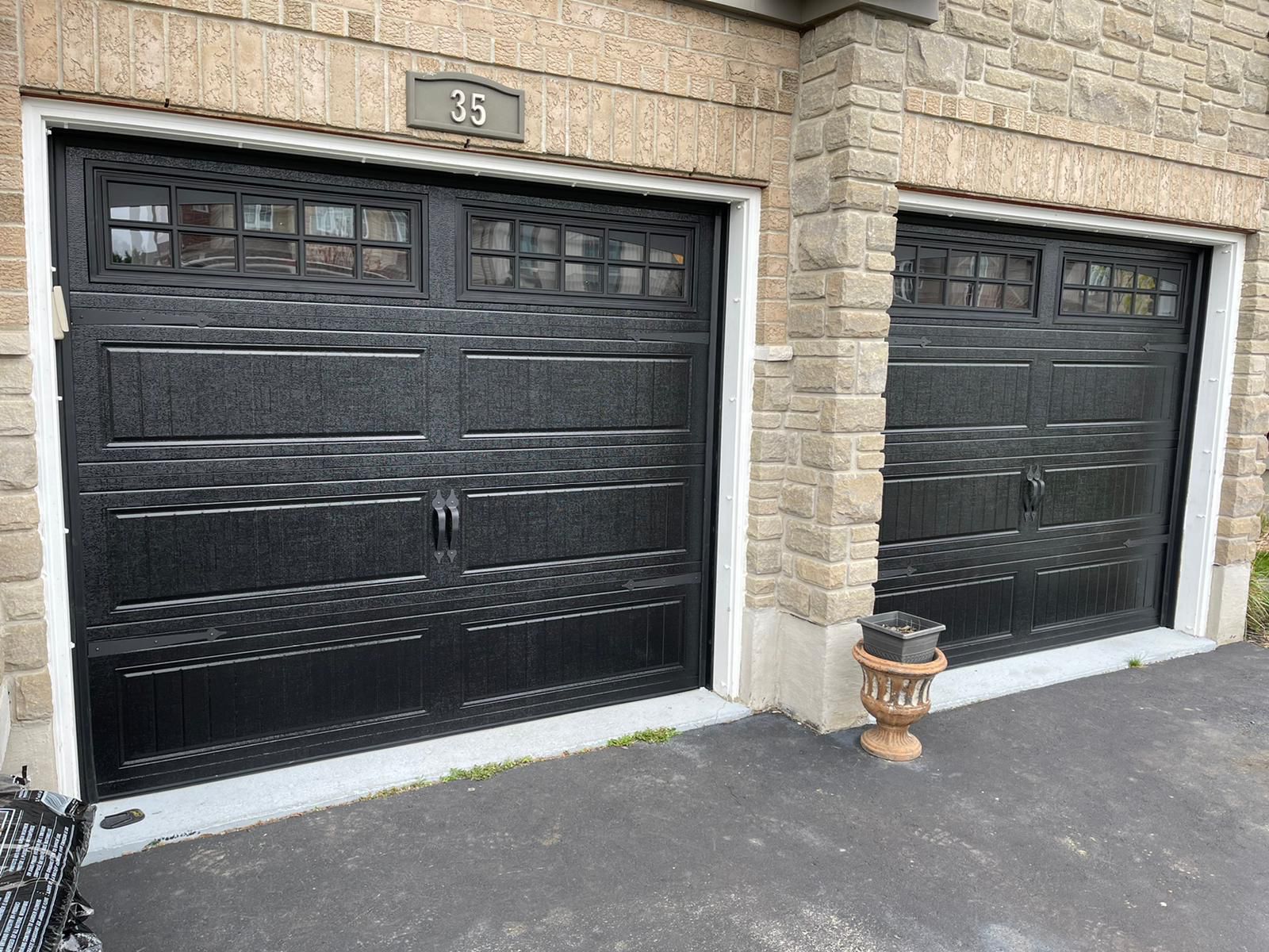 Two black classic raised-panel garage doors with top windows at house 35 on a stone-clad home