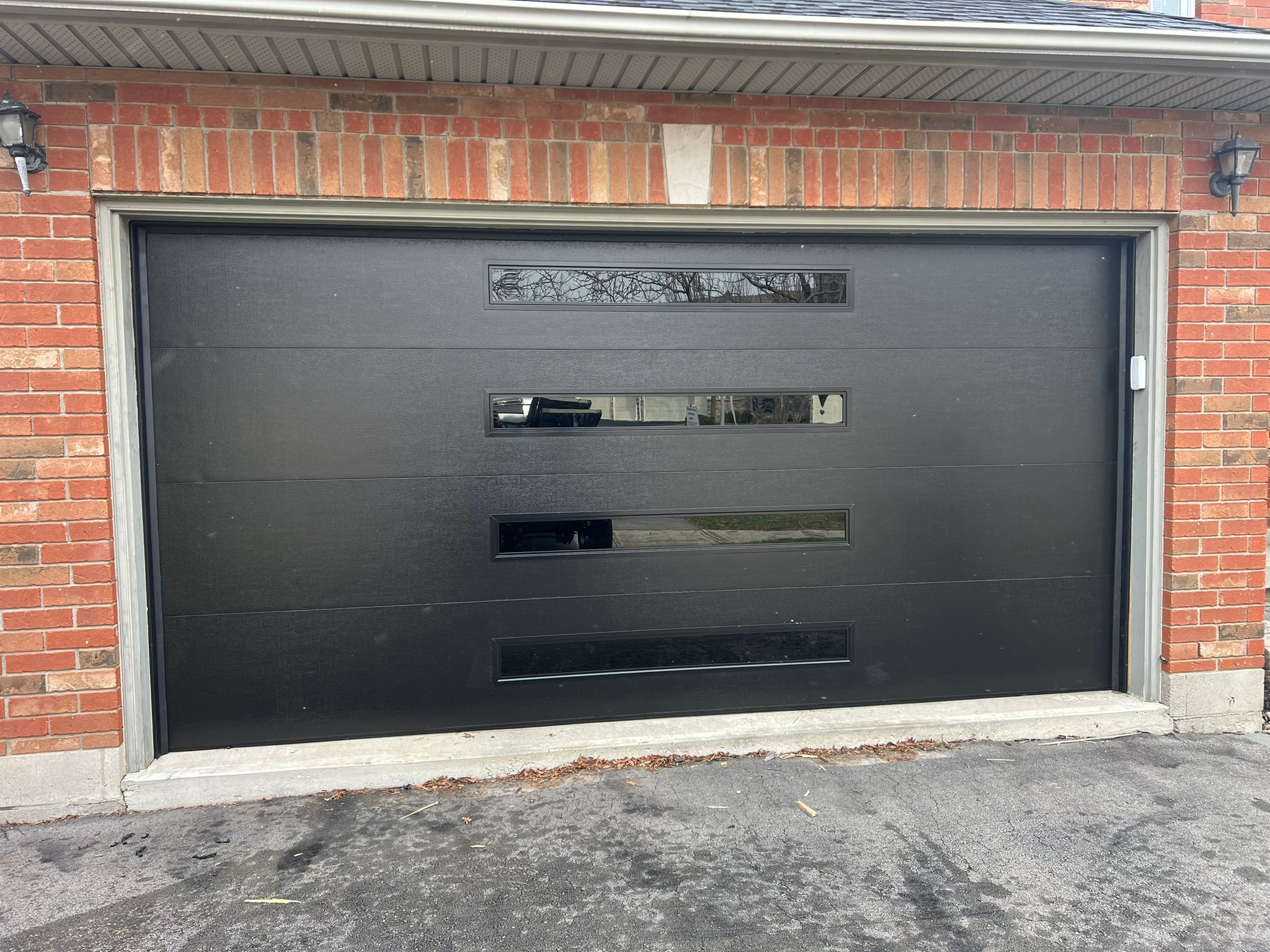 Black horizontal-panel contemporary garage door with top windows on a red brick home