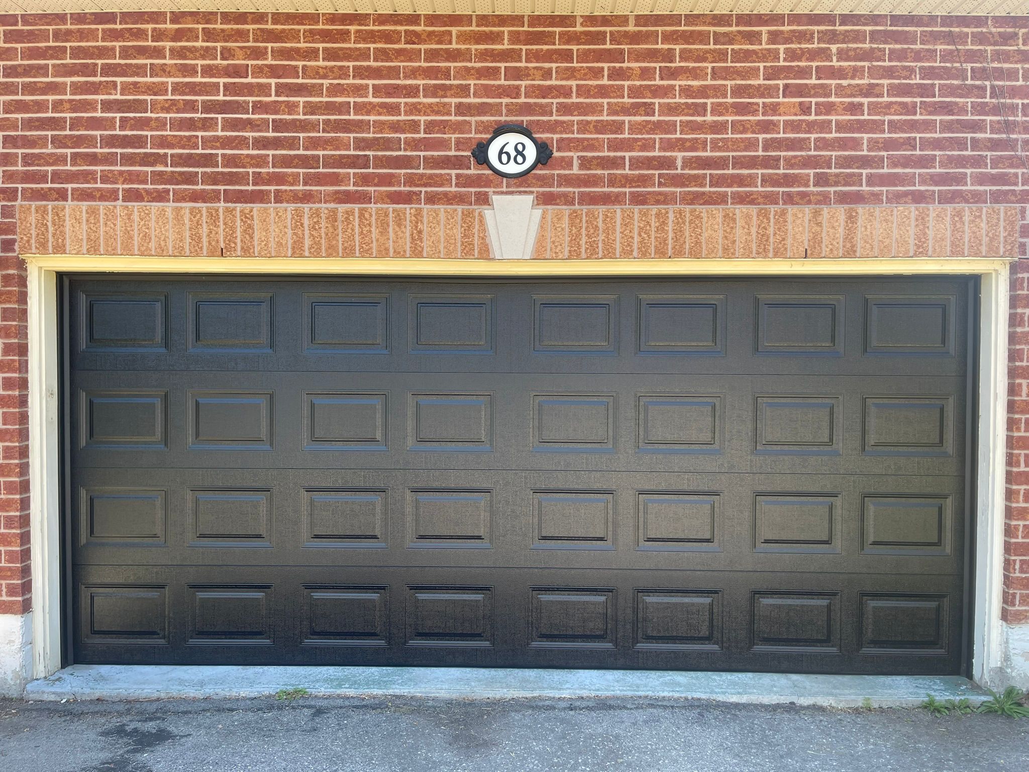 Wide black raised-panel double garage door at house 68 on red brick