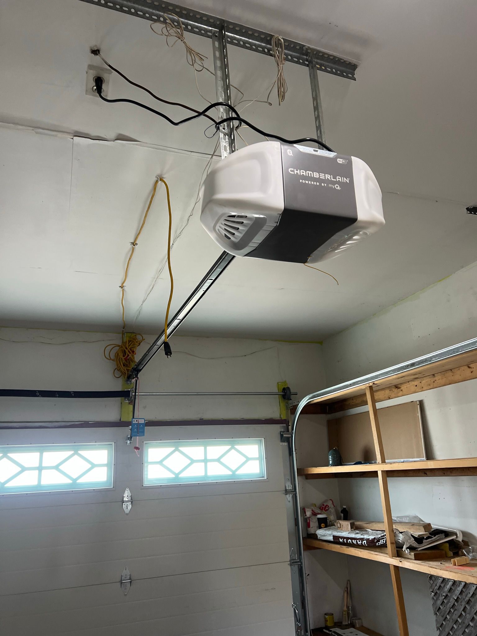 Chamberlain garage door opener installed on a garage ceiling with spring cable and wiring visible