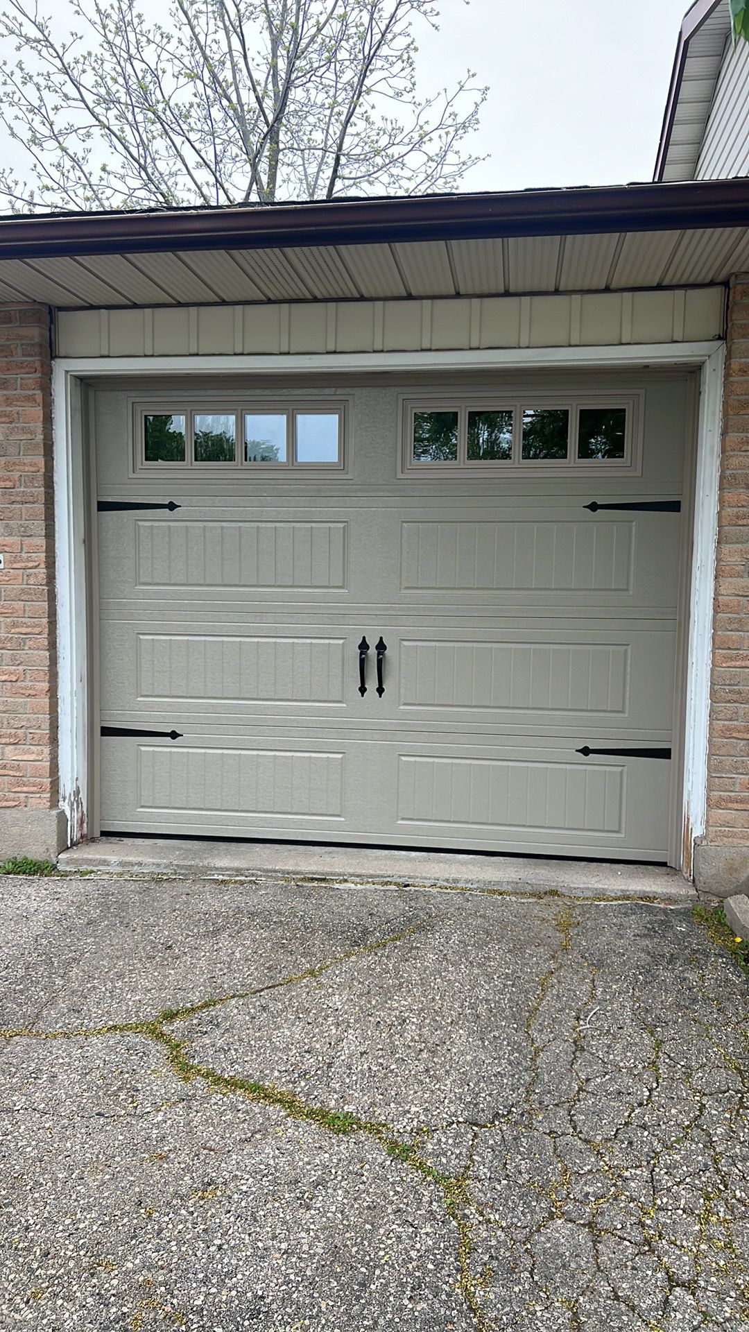 Cream white carriage-style single garage door with decorative black hardware and top windows on a light garage
