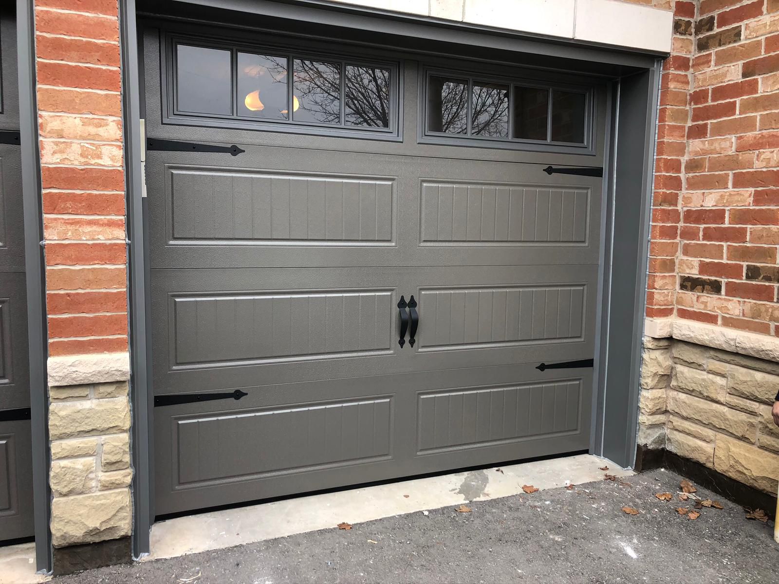 Grey single carriage-style garage door with decorative strap hinges and handles on a red brick home