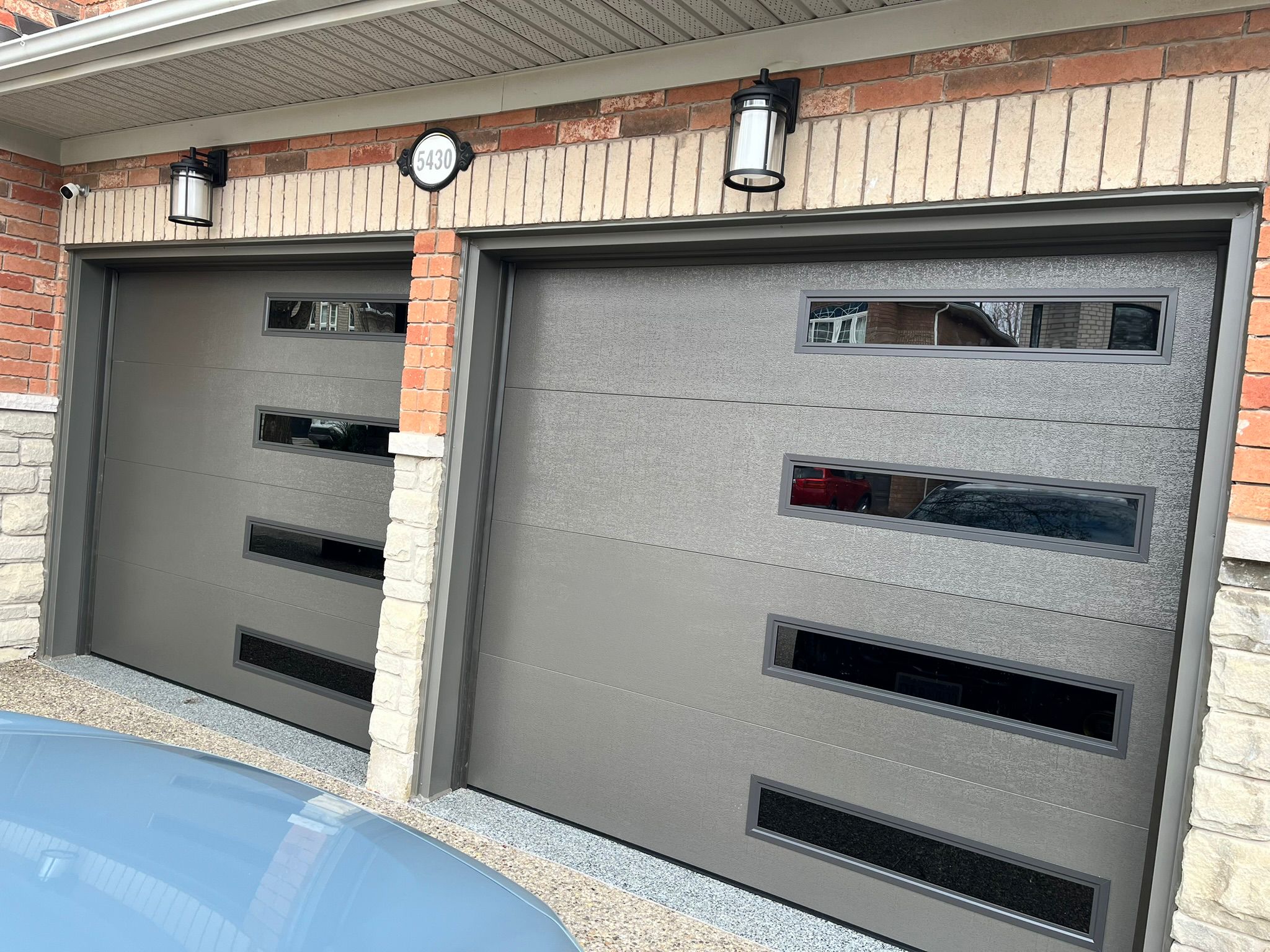 Two grey contemporary horizontal-panel garage doors with windows at house 5430
