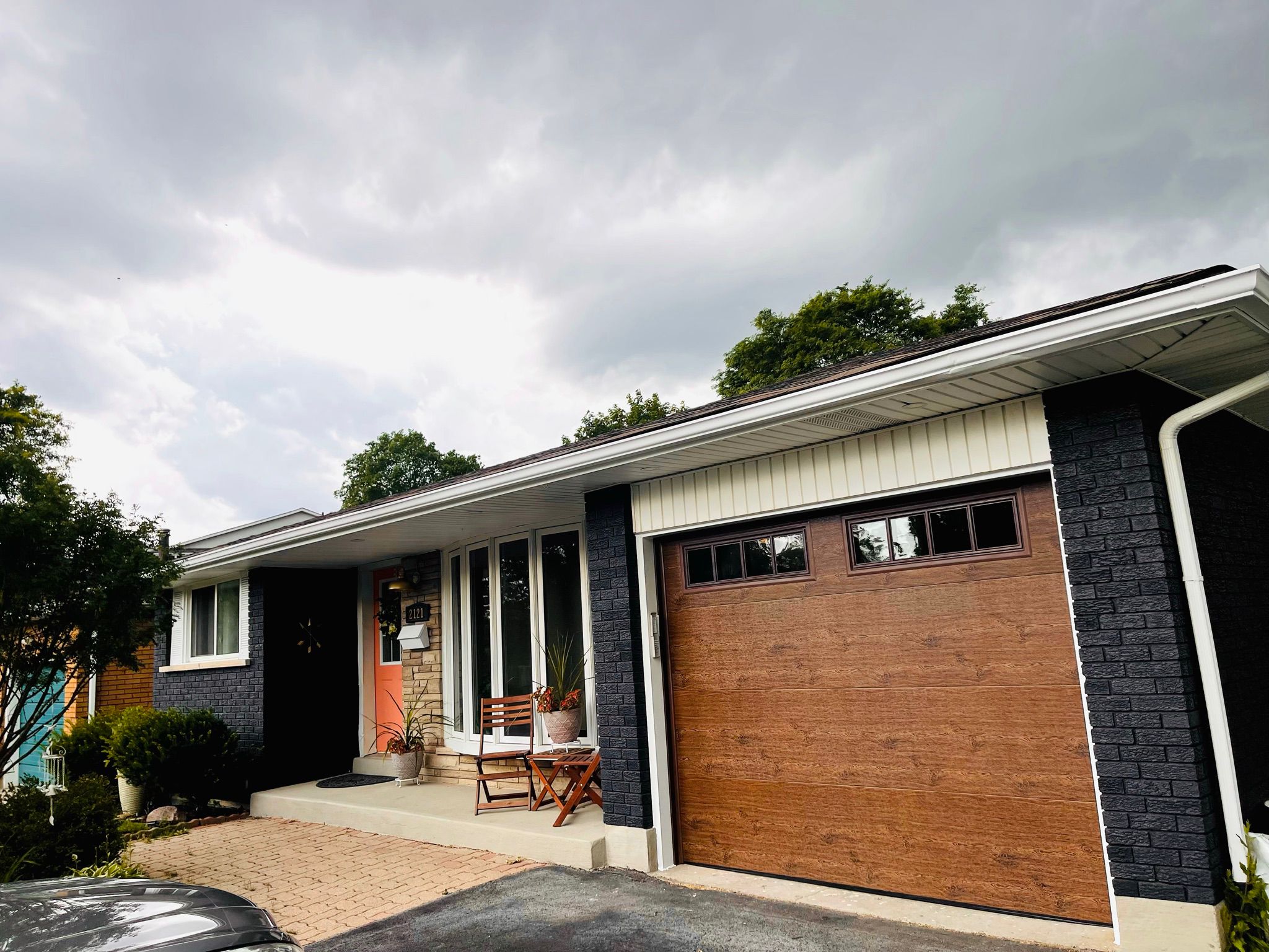 Honey-finish faux-wood single garage door with top windows on a dark painted brick home, wide curb-appeal view