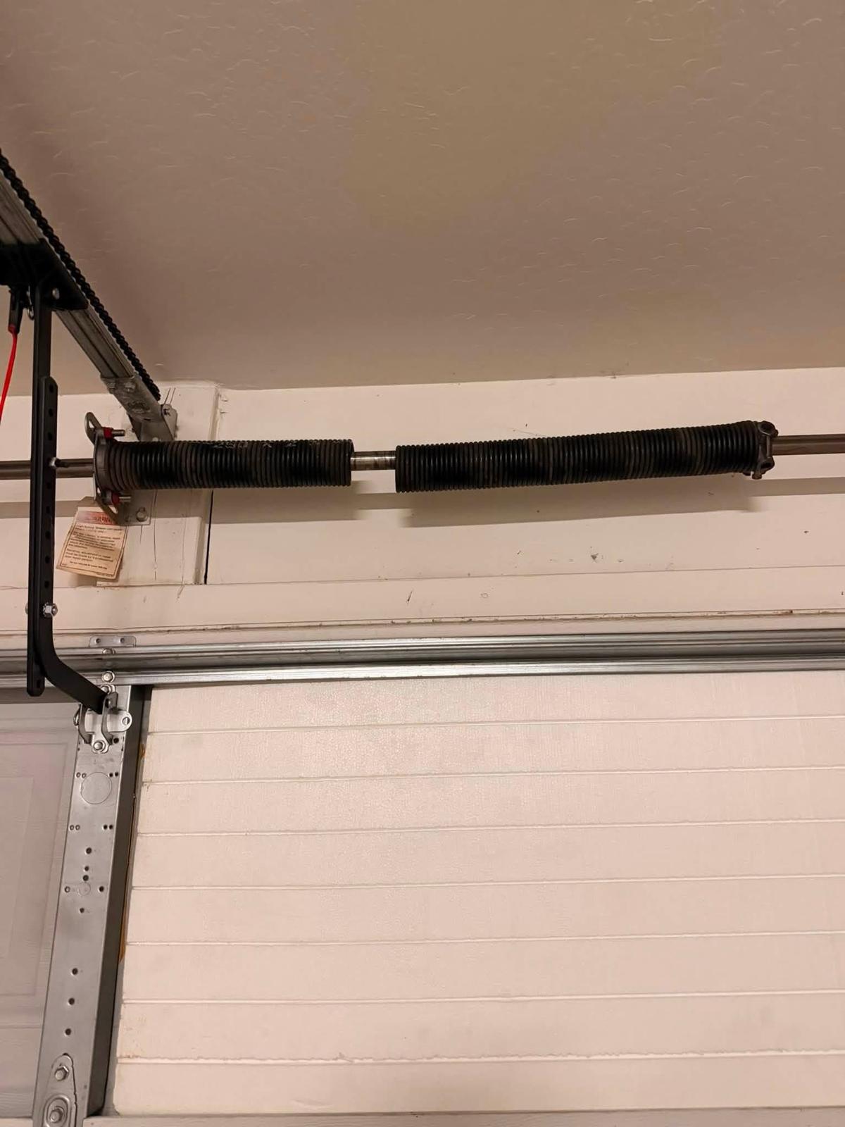 Broken torsion spring with visible gap on the shaft above a white garage door - LTA field photo
