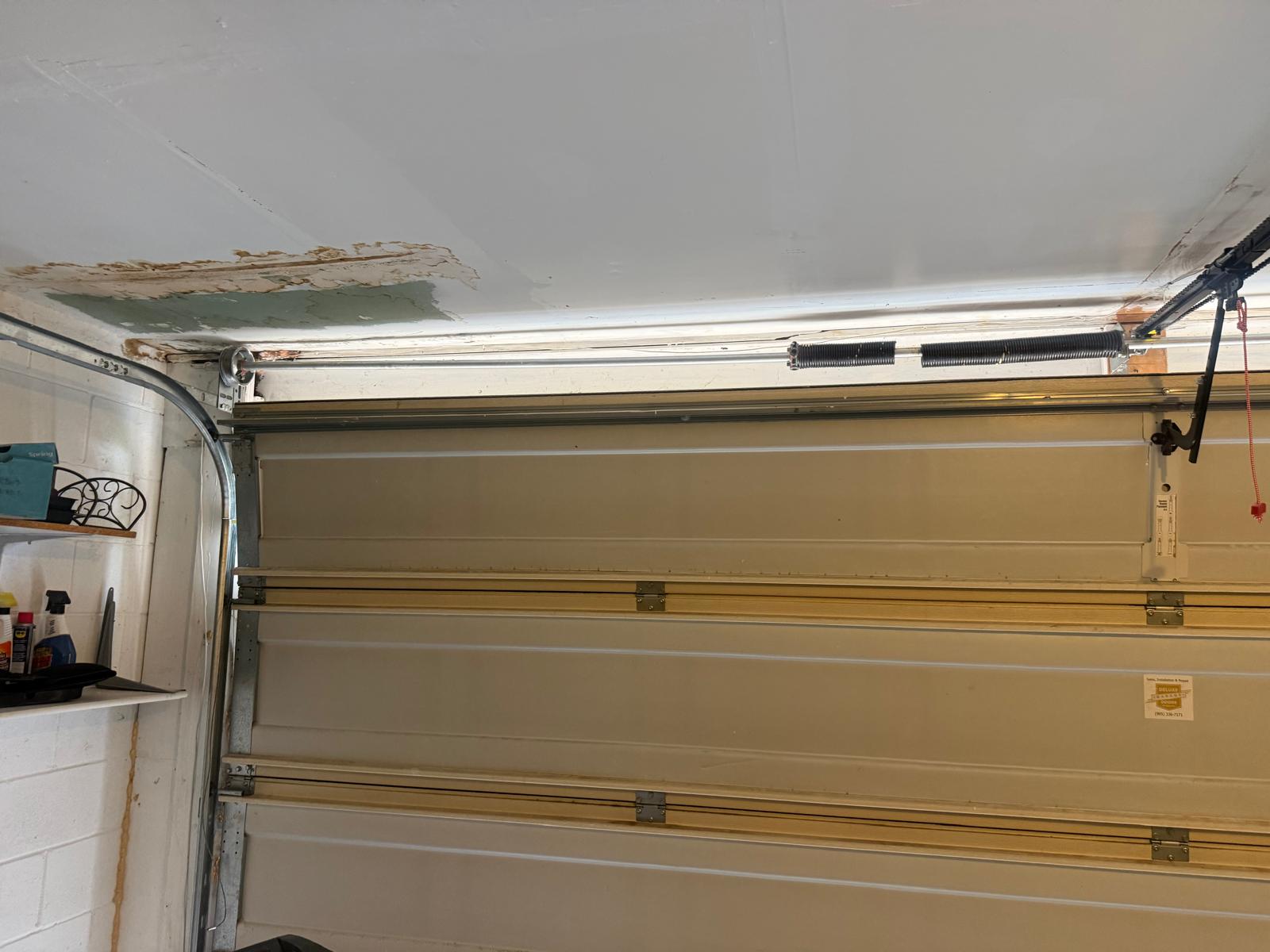 Residential garage door torsion spring assembly and cable drum above a white sectional door - LTA field photo