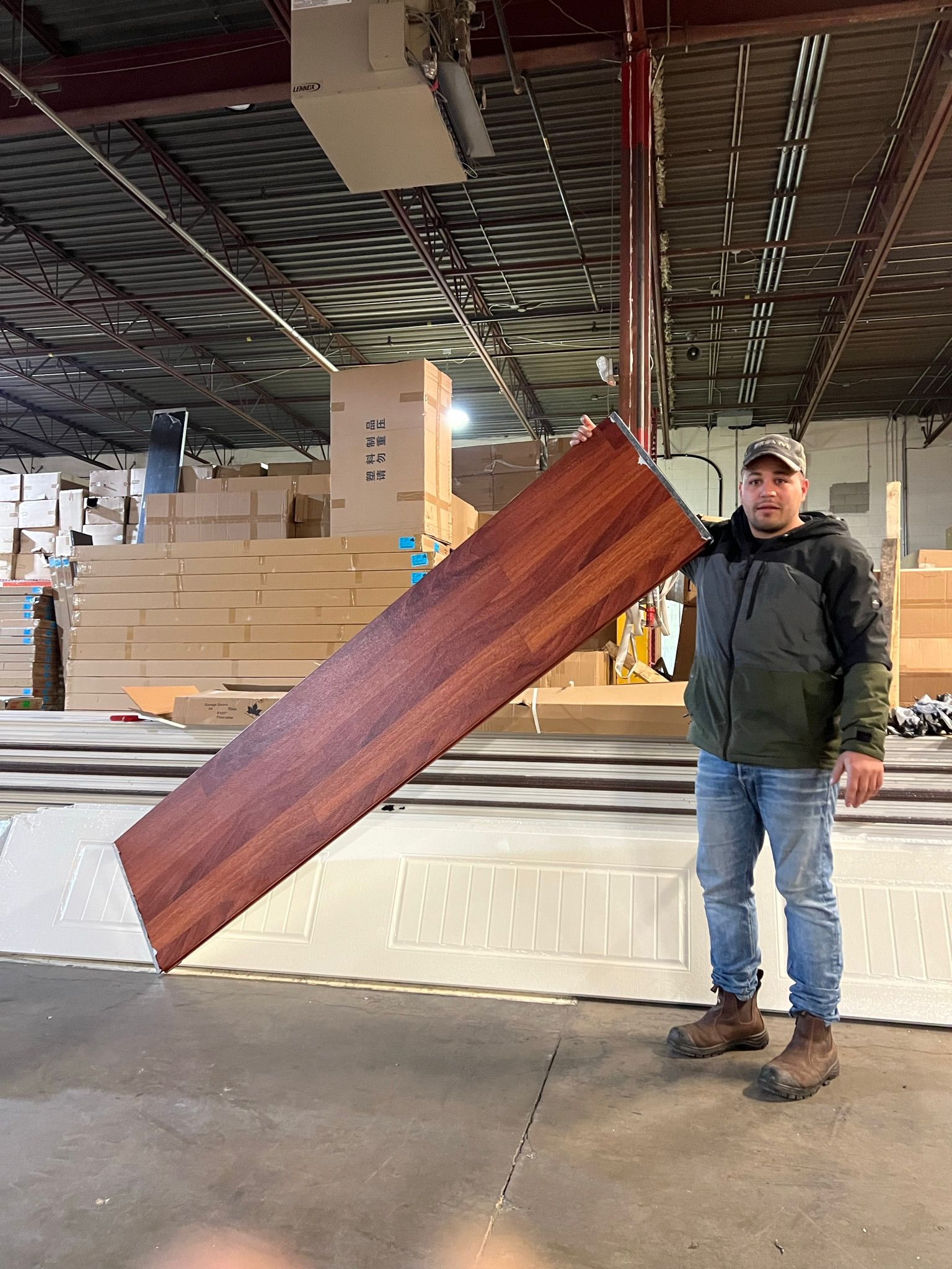 LTA Garage Doors technician holding a walnut-finish garage door panel in a supply warehouse