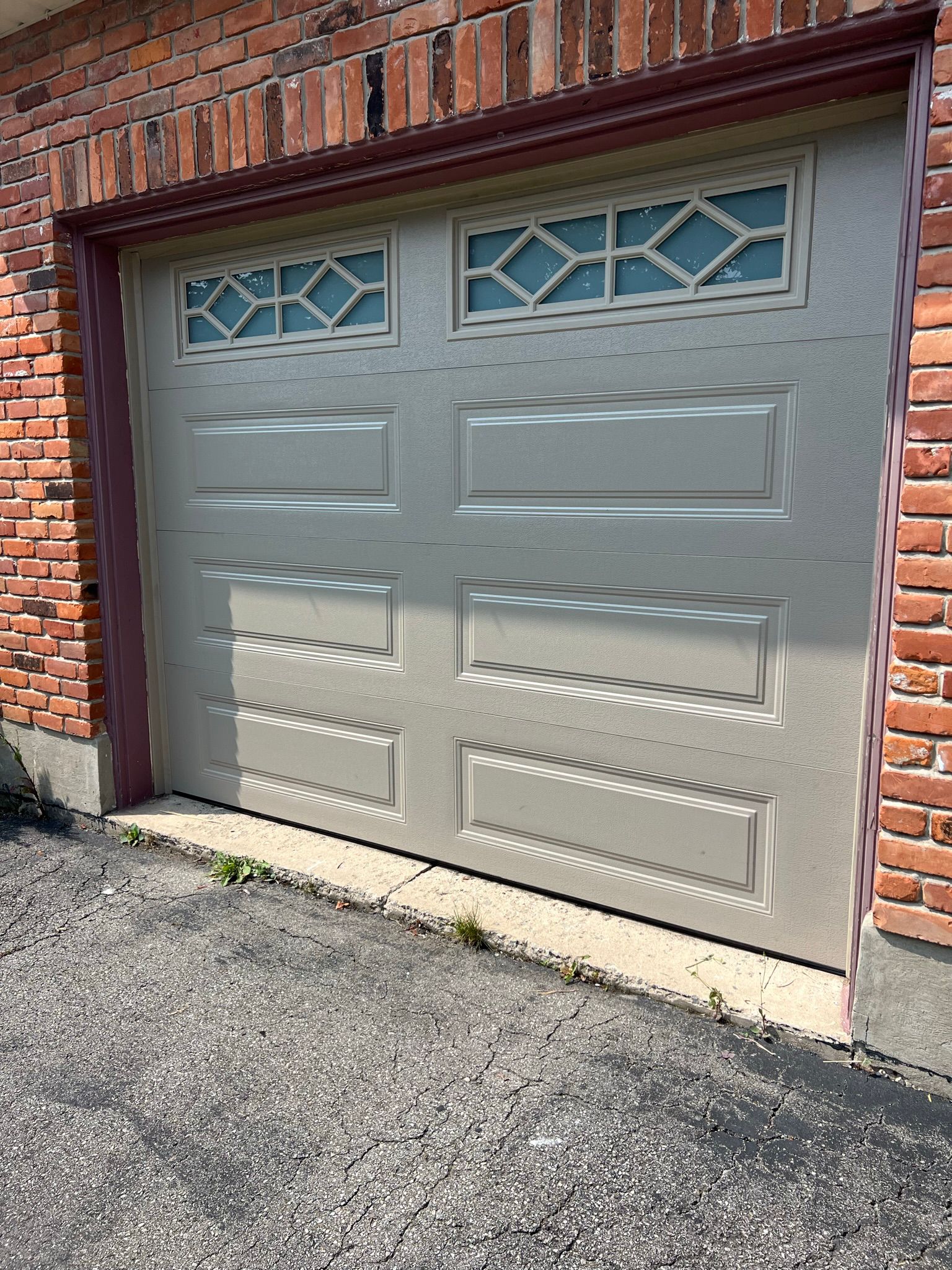Sage-green classic single garage door with decorative diamond-pane top windows on red brick