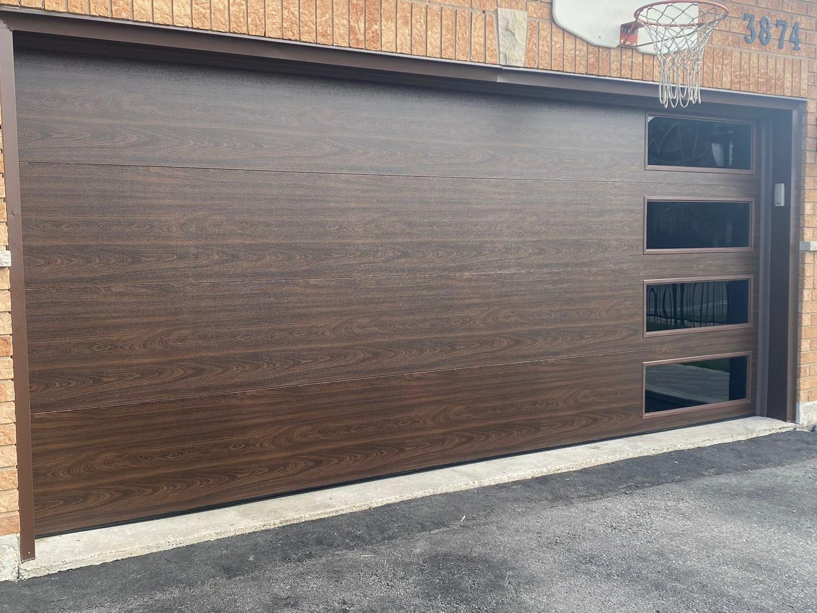 Dark walnut-finish wide garage door with horizontal panels and a glass column sidelight at house 3874 on brick